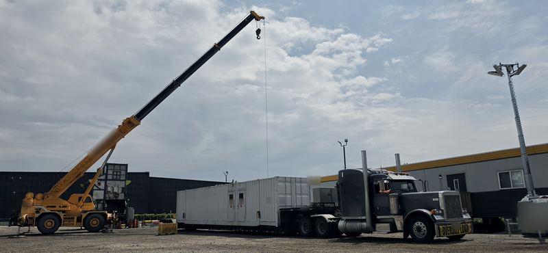 Crane loading a long modular unit onto a lowboy behind a Peterbilt 379 with an oversize-load banner