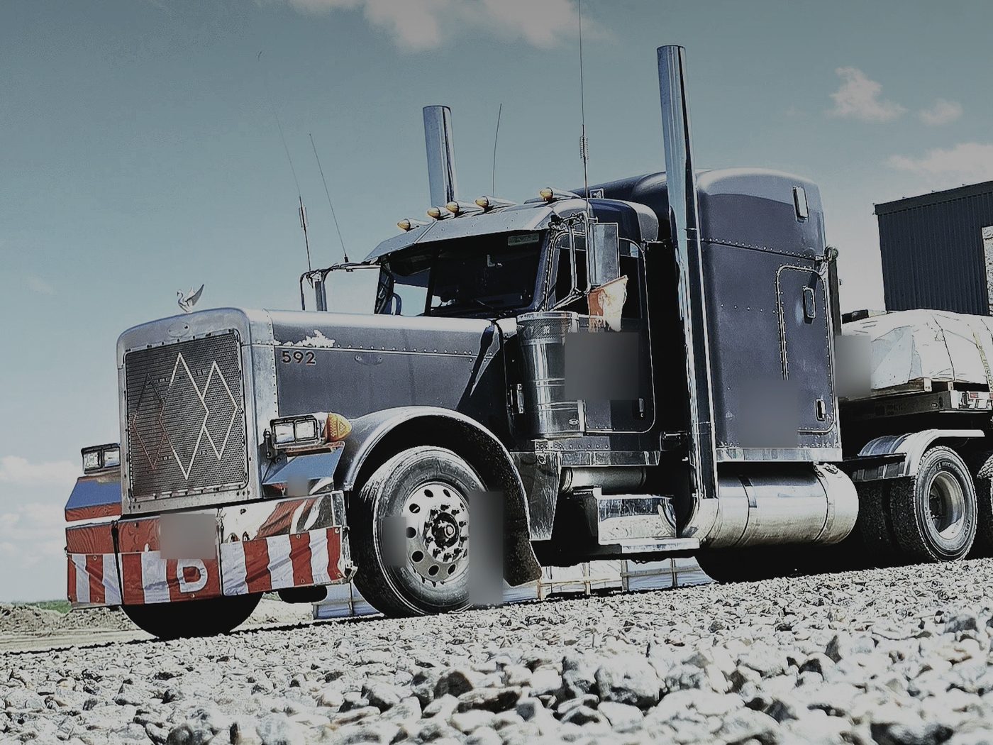 Low-angle view of a long-nose Peterbilt 379 with tall stacks pulling a multi-axle lowboy loaded with a modular building